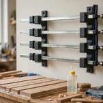A bright home workshop scene, matte charcoal-gray 3D printed bar clamp rack brackets on a wall holding four long bar clamps flat and parallel