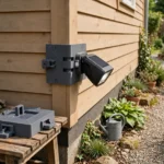 A bright home exterior scene with a matte charcoal-gray 3D printed corner mount fitted around the corner of a house wall holding a sealed black solar