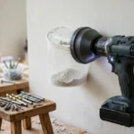 A bright home interior workshop scene, a cordless drill fitted with a matte dark-gray 3D printed dust shroud adapter and a translucent dust cup