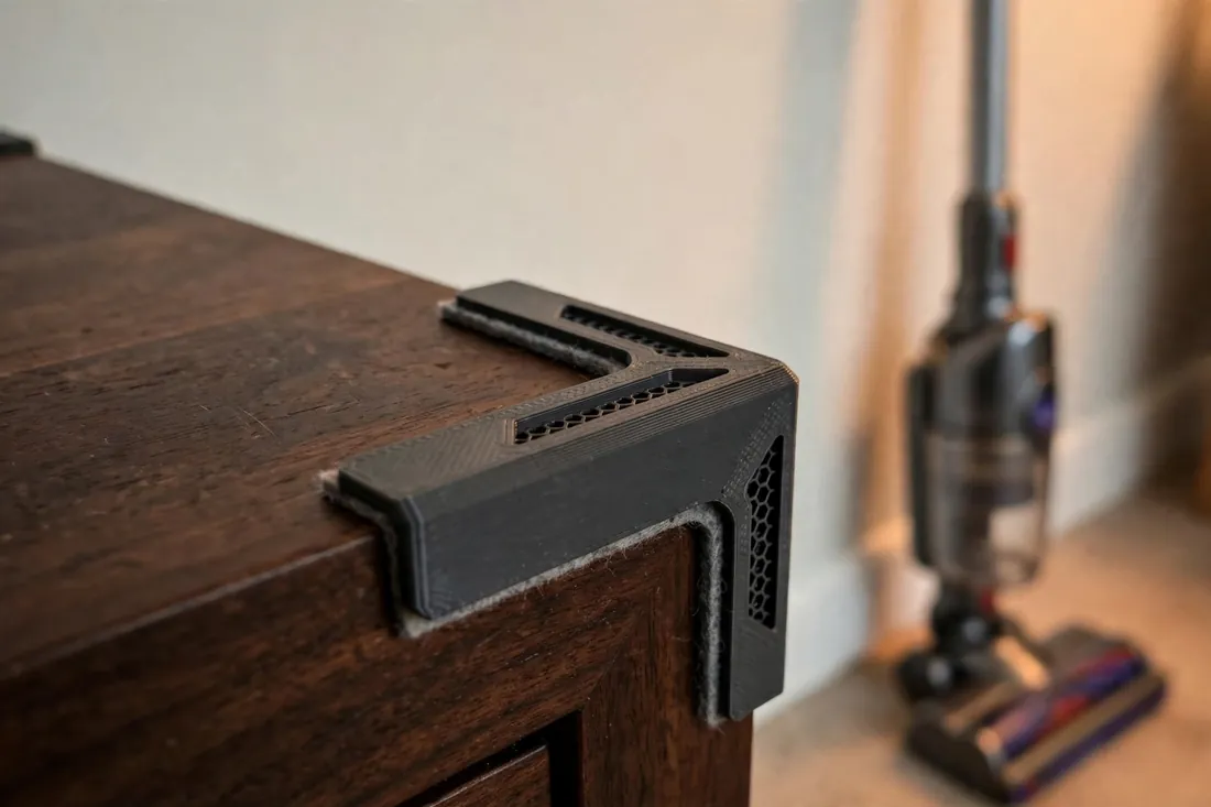 Close-up view of a dark walnut side table corner wearing a charcoal-gray 3D printed corner protector with a thin felt lining visible at its edge