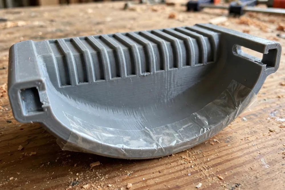 Close-up of a single 3D printed glue up caul on a workbench, showing its gently cambered bottom face, ribbed top