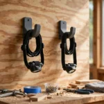 A bright home workshop wall with two headlamps hanging from matte charcoal-gray 3D printed wall hooks on a plywood panel