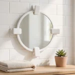 A bright bathroom wall scene, a small round mirror with a plain frame held by four matte white 3D printed mirror clips at its edges