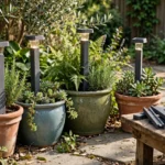 A patio scene with terracotta and glazed planters holding solar lights on matte charcoal-gray 3D printed planter stakes among the foliage