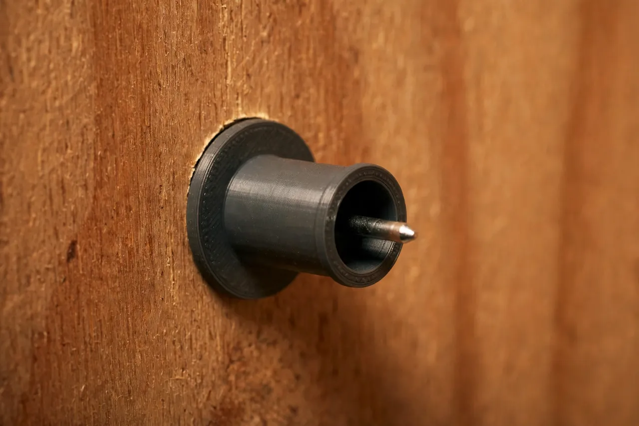 Close-up of a charcoal-gray printed shelf pin sleeve pressed into a cabinet side hole with a metal 1/4-inch shelf pin inserted