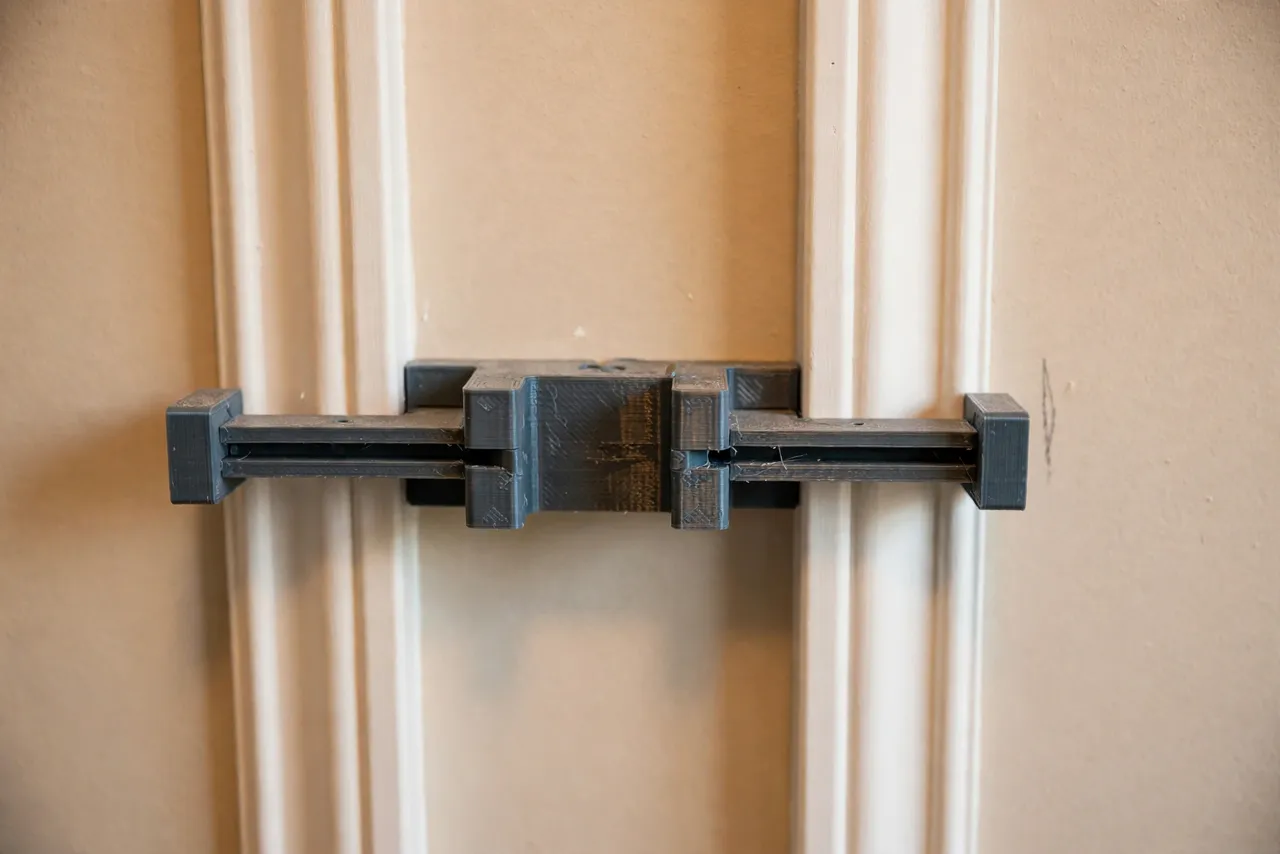 Close-up view of a 3D printed spacing jig with two spacer arms setting an even gap between two white wainscot stiles on a wall
