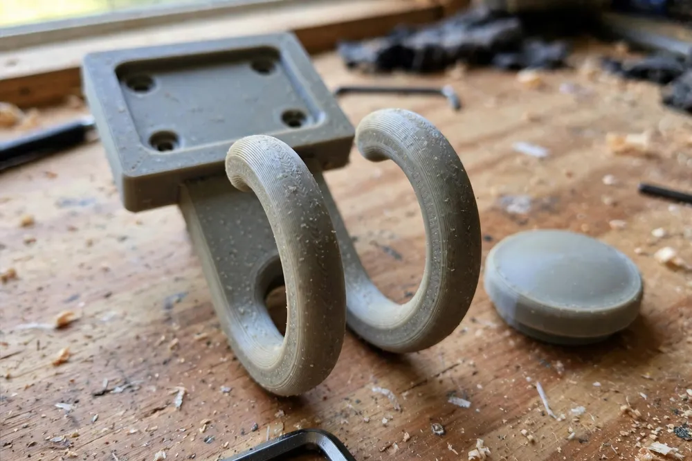 Close-up of a single 3D printed double wall hook on a workbench showing its concealed-screw mounting plate