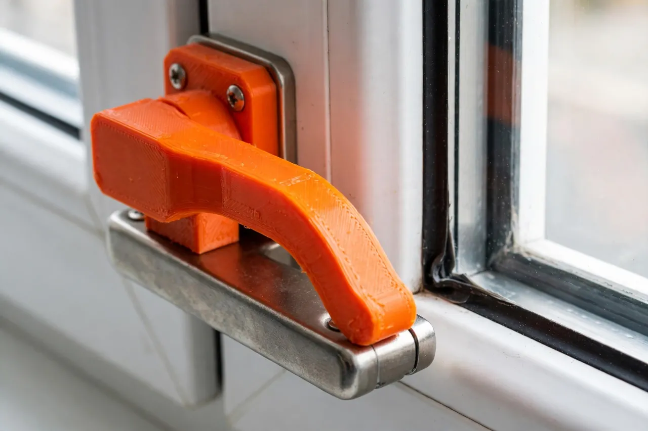 Close-up of a bright-orange 3D printed window latch handle mounted on a window frame