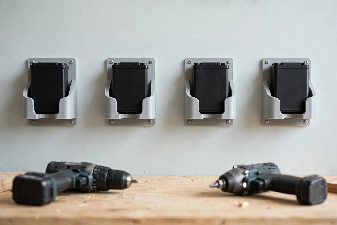 A tidy row of four matching 3D printed battery cradles mounted on a painted workshop wall