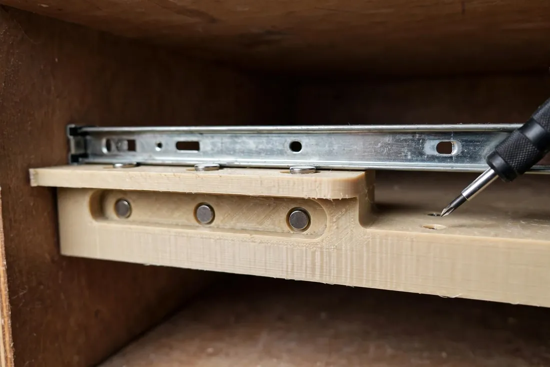 Close-up side view inside a cabinet showing the flat support ledge of a 3D printed jig cradling the underside of a metal drawer slide